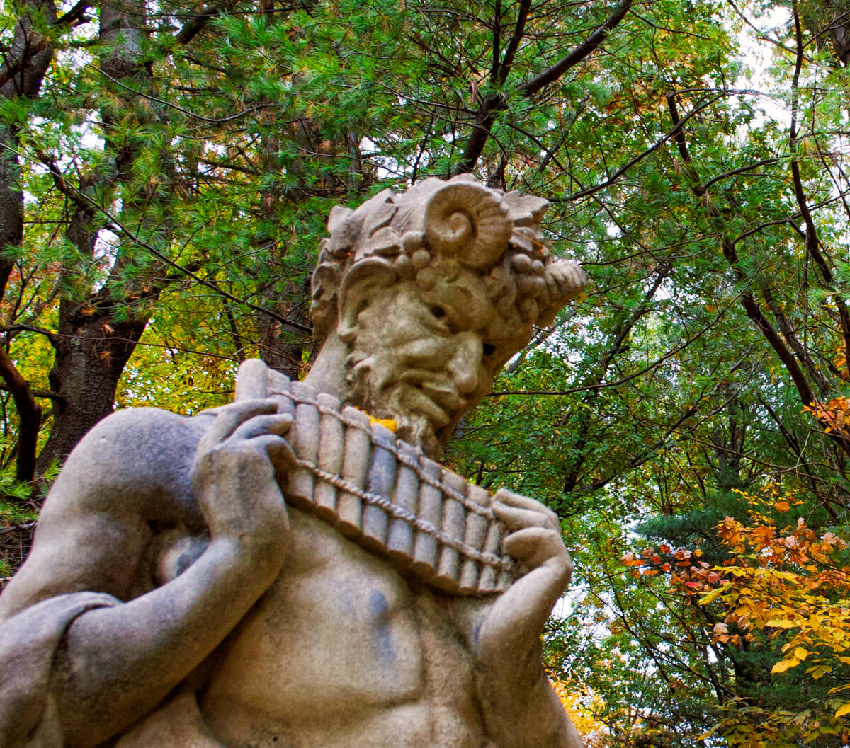 A Forgotten Song A statue of Pan with pipes in hand against an autumn forest of deciduous and fir trees.