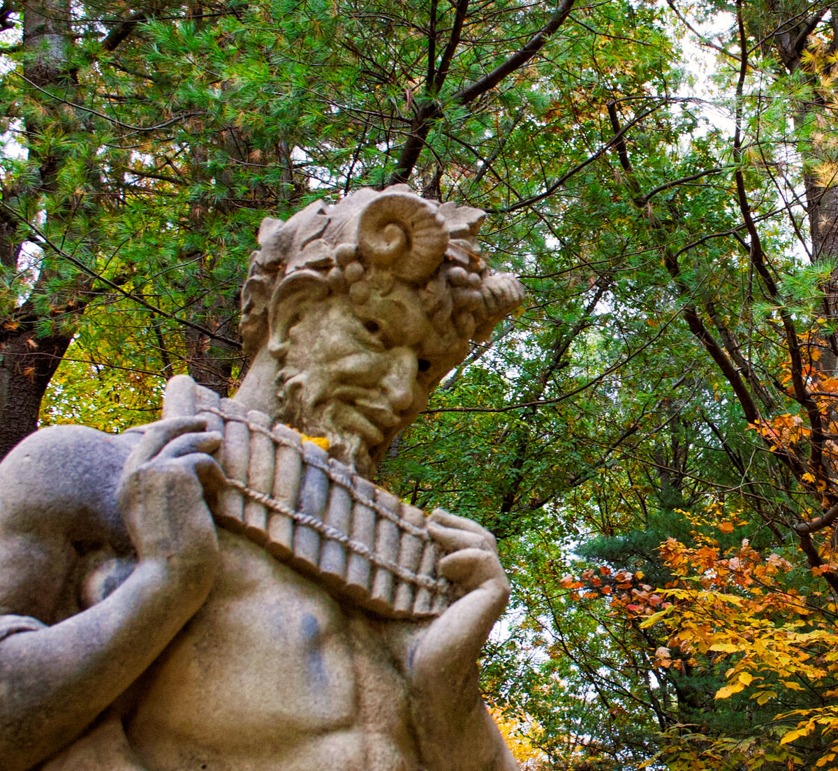 A Forgotten Song A statue of Pan with pipes in hand against an autumn forest of deciduous and fir trees.