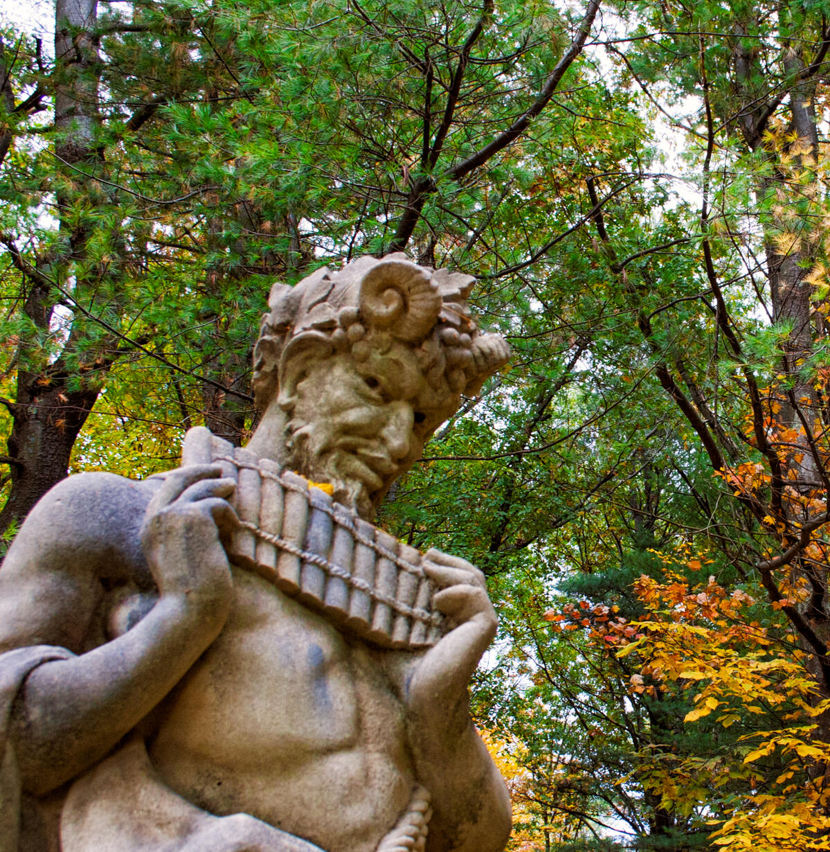 A Forgotten Song A statue of Pan with pipes in hand against an autumn forest of deciduous and fir trees.