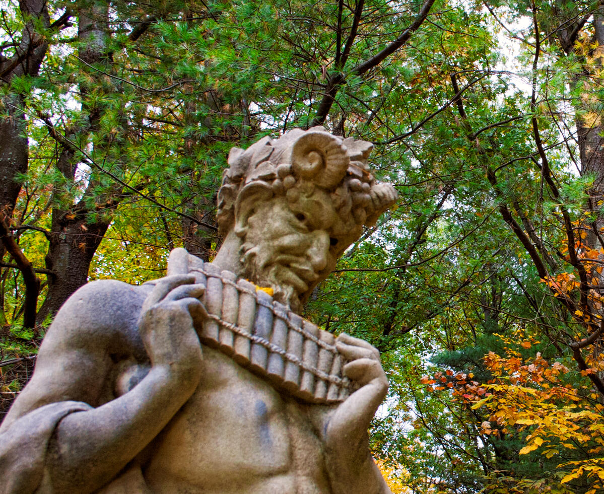 A Forgotten Song A statue of Pan with pipes in hand against an autumn forest of deciduous and fir trees.