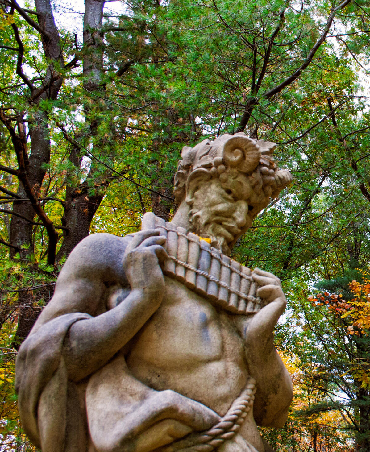 A Forgotten Song A statue of Pan with pipes in hand against an autumn forest of deciduous and fir trees.